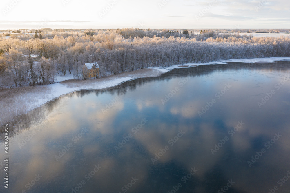 Aerial drone view of a lake coast starting to freeze over in winter sunrise light. Tartu, Estonia.