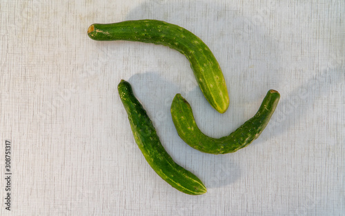 Three misshapen cucumbers on the white with gray stripes rustic table. Natural cucumbers are healthy food, which contains lot of vitamins good for diet. Horizontal orientation Image, light background.