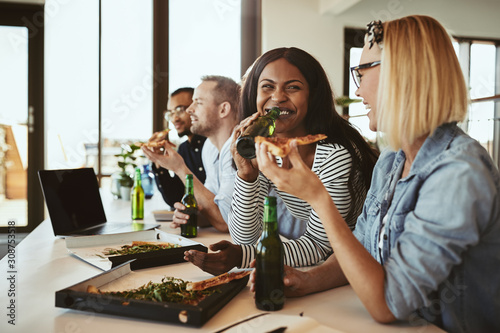 Laughing businesswomen having pizza and beer with colleagues aft