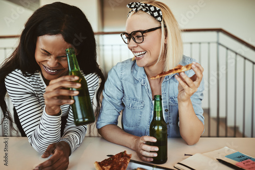 Laughing young businesswomen drinking beers and having pizza aft