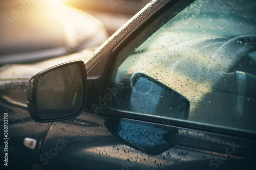 The rain-soaked windows and mirrors of the  car, which are illuminated by the light of the sun that has just come out from behind the clouds.