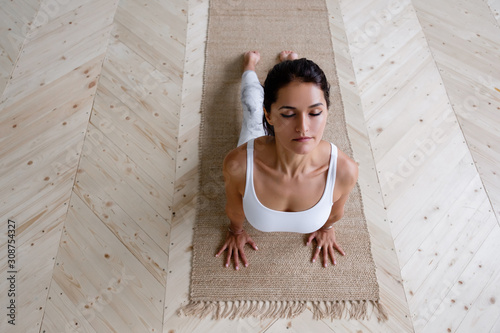 Top view of a beautiful pacific caucasian woman yoga teacher doing urdhva mukha shwanasana with eyes closed on a rug on the floor in a cozy home atmosphere. Yoga and Pilates concept. Advertising space photo