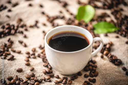 A mug of strong black coffee and scattered grains. Fragrant invigorating drink from freshly roasted coffee beans