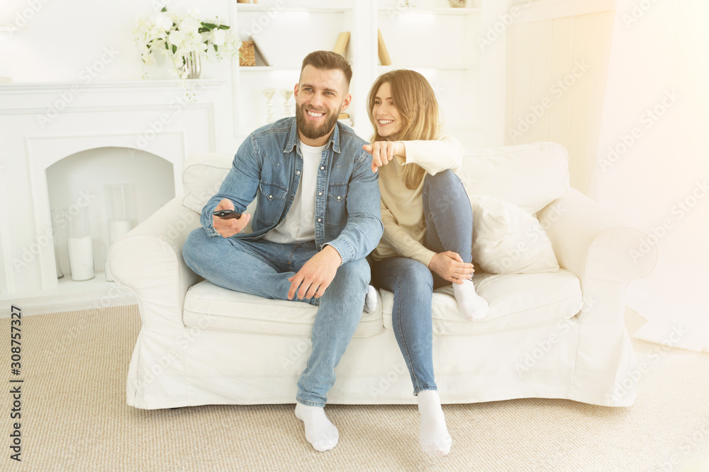 Relaxed couple watching TV at home, woman pointing on screen