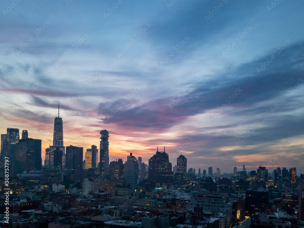 Dusk falls over the downtown Manhattan skyline with the lights of the skyscrapers contrasted against the colorful evening sunset sky in New York City