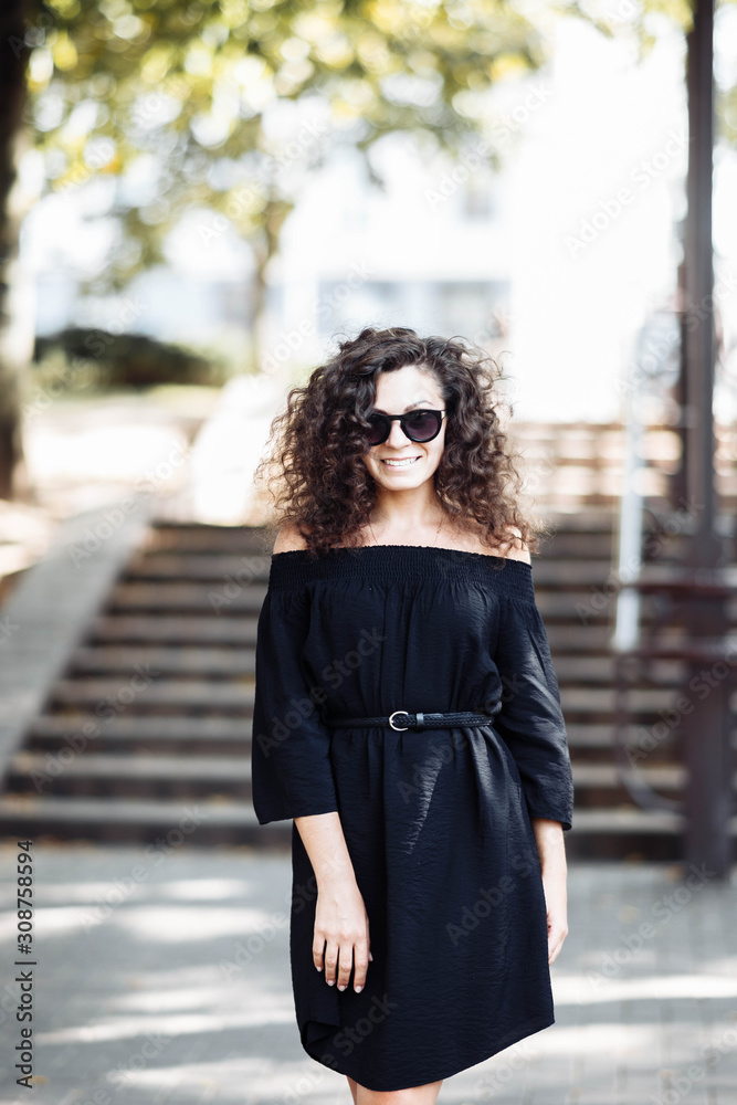 Fototapeta premium Portrait of a curly young brunette woman in sunglasses on a sunny summer day.