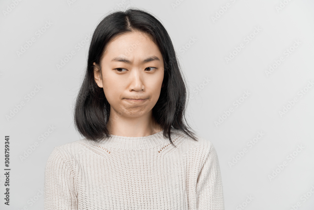 Thoughtful pensive pretty young female looks doubtfully aside, being deep in thoughts. Businesslike young woman Asian appearance dressed in knitted warm sweater stands isolated white background Thoughtful pensive pretty young female looks doubtfully aside, being deep in thoughts. Businesslike young woman Asian appearance dressed in knitted warm sweater stands isolated white background