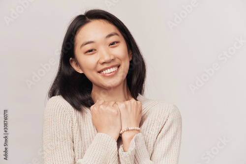 Kind friendly young pretty woman keeps palms on heart, being positive and kind hearted, expresses good feelings to close person. woman dressed in knitted warm sweater stands isolated white background