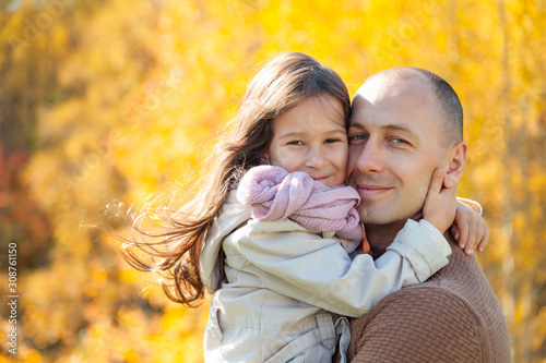 Man caucasian dad in sunglasses hugs beautiful daughter on background of colorful autumn trees. Concept family weekend, love, relaxing outdoors, fun, people, season, weather, picturesque forest