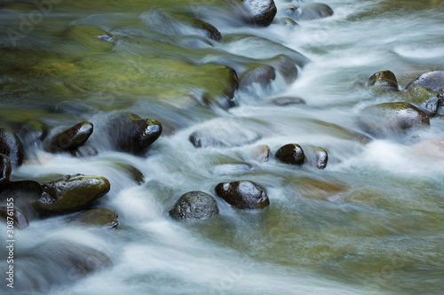Landscape of the Little River captured with motion blur and illuminated by reflected color from sunlit foliage and blue sky overhead, Great Smoky Mountains National Park, Tennessee, USA