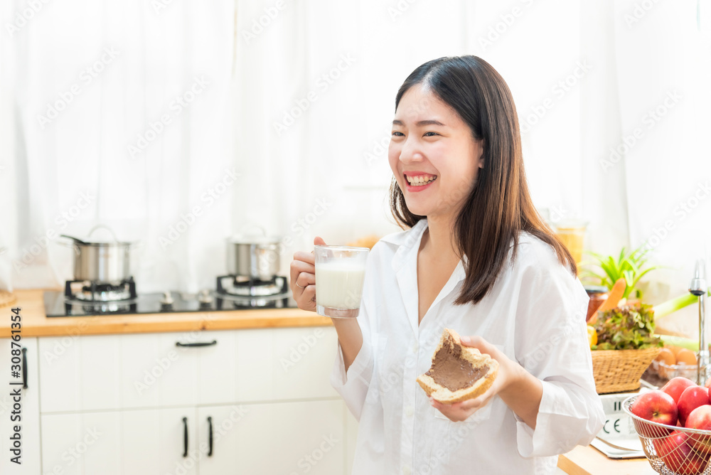 Happy young girl eating bread with a glass of milk for breakfast in kitchen. Healthy eating and lifestyle concept. Happy young girl eating bread with a glass of milk for breakfast in kitchen. Healthy eating and lifestyle concept.