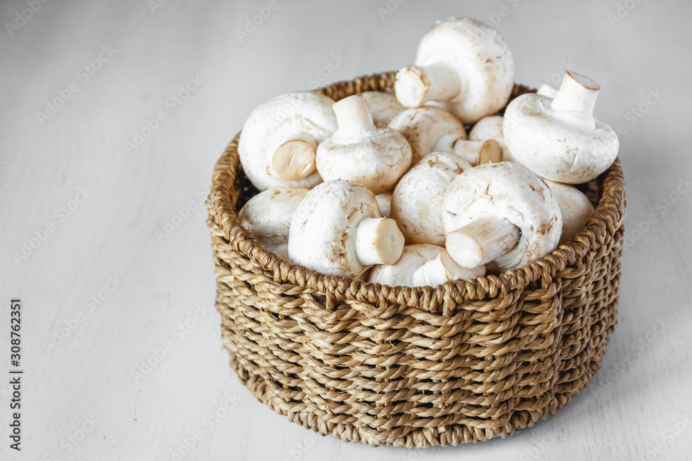 Mushrooms champignons in a round wicker basket on a white wooden table. Place for text or advertising
