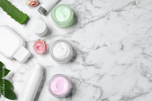 Flat lay composition with jars of organic cream and flowers on white marble table. Space for text