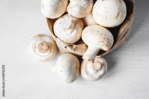 Mushrooms champignons in paper bag on a white wooden table. Close up. Place for text or advertising