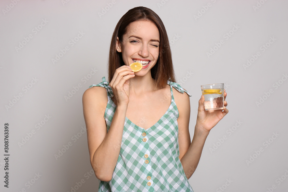 Young woman with glass of lemon water on light background Young woman with glass of lemon water on light background
