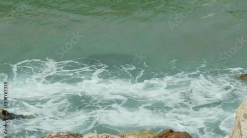 Close up shot of blue and green waves of a beautiful sea crushing onto stones of a sea shore. Slow motion 4K photo