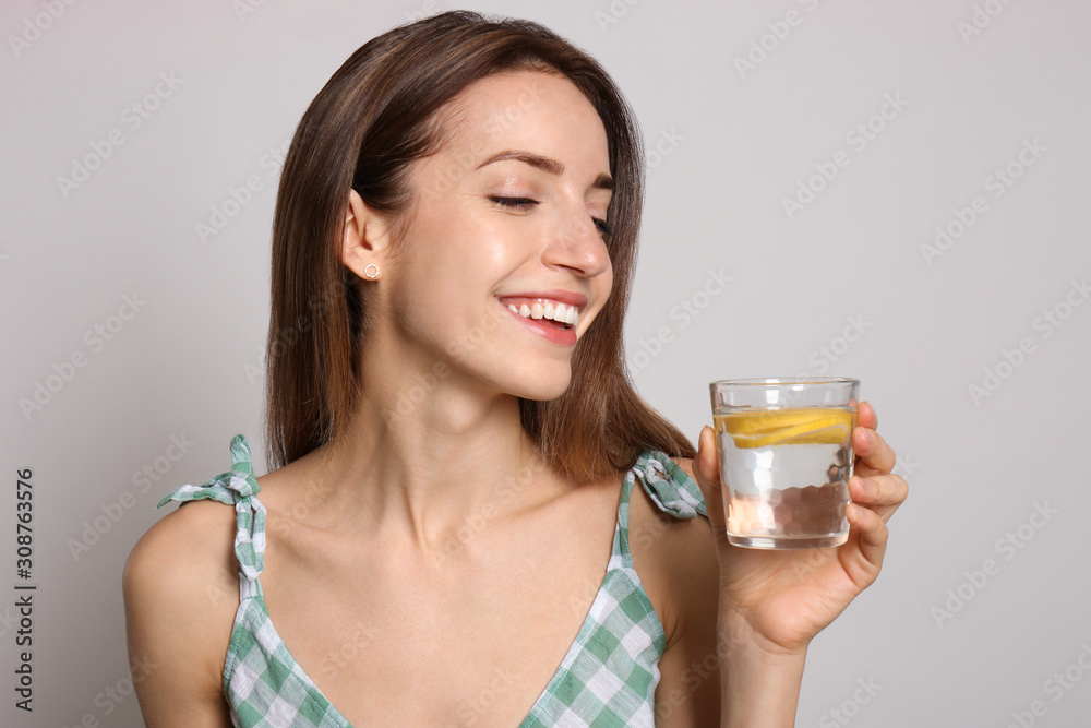 Young woman with glass of lemon water on light background Young woman with glass of lemon water on light background