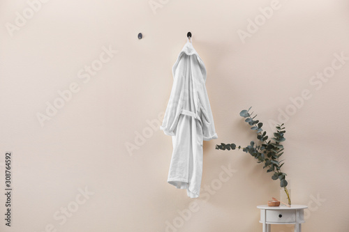 Soft comfortable bathrobe hanging on beige wall indoors, space for text