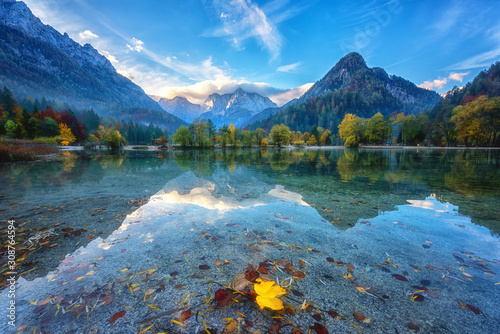 Fototapeta Naklejka Na Ścianę i Meble -  Jasna lake in Triglav national park at sunrise, Kranjska Gora, Slovenia. Amazing autumn landscape with Alps mountains, trees, blue sky with clouds and reflection in water, famous tourist attraction