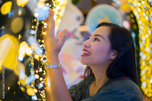 Young Asian woman posing against the backdrop of a Christmas tree with garlands to night. Outdoor Christmas decoration photo