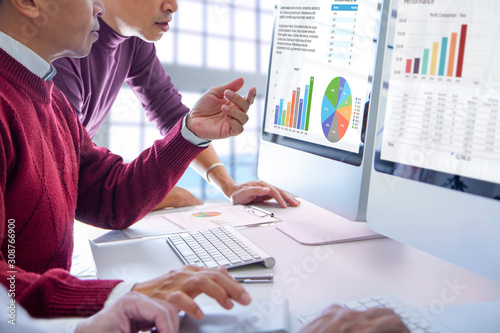 Business men looking into modern computer screens reviewing business performance and return on investment, ROI, with colorful graphs.
