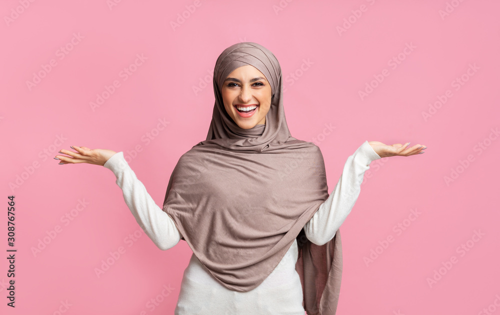Joyful muslim woman in hijab demonstrating something on her empty palms Joyful muslim woman in hijab demonstrating something on her empty palms