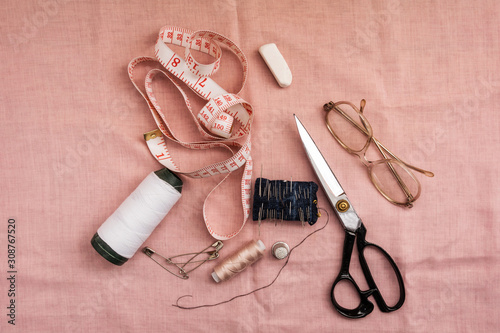 Sewing tools lie on pink fabric. Needles, threads and scissors are prepared for the job.
