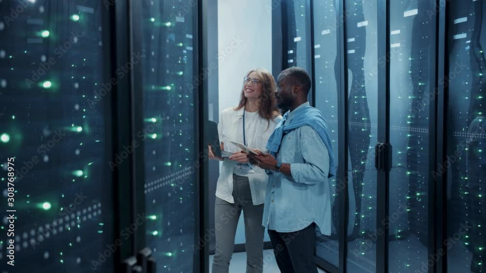 Attractive team of multi-ethnic colleagues working inside futuristic server room. Positive diverse man and woman specialists smiling having fun together in data center. Attractive team of multi-ethnic colleagues working inside futuristic server room. Positive diverse man and woman specialists smiling having fun together in data center.