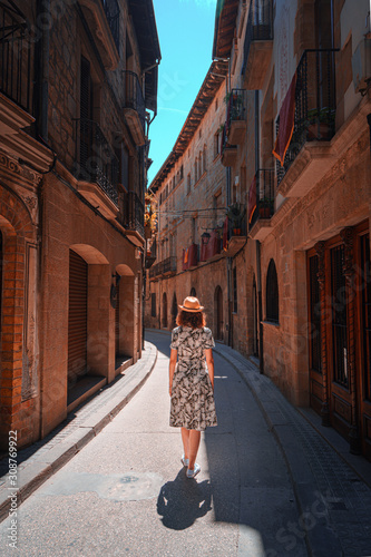 Rear view of a young woman walking in a narrow and old street of Solsona, Spain. Teal and orange