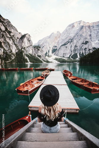 Traveler young girl in hat sits on the pier and enjoying the beautiful nature lake at Lago di Braies Dolomites Italy