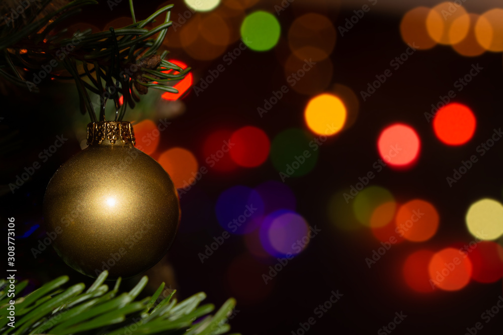 Golden bauble hanging in a Christmas tree, with bright colorful bokeh light spots on the background