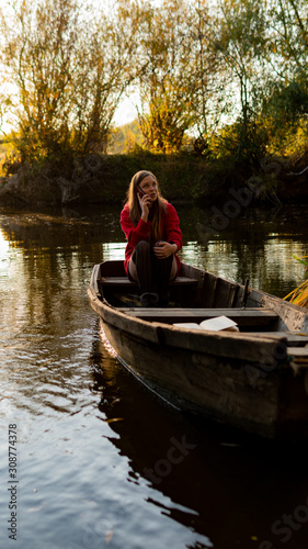 curly girl sitting on the edge of an abandoned wooden boat at sunset. © Oleksandr