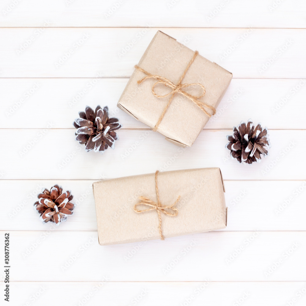 Christmas gifts in craft packaging with pine cones on white wooden background. Festive composition, square Christmas gifts in craft packaging with pine cones on white wooden background. Festive composition, square