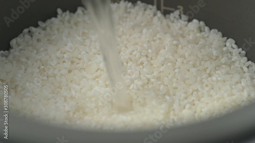 Making Japanese sushi rice, pouring water into rice bowl inside rice cooker.