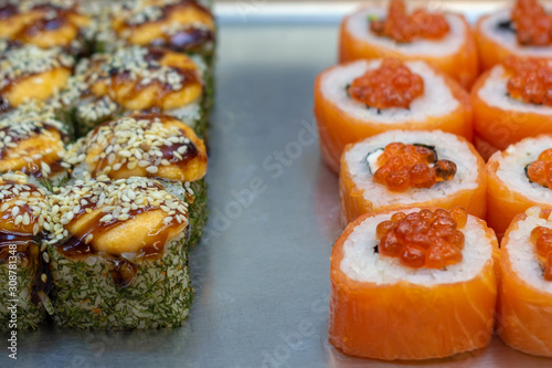 Two kinds of sushi rolls on metal plate. With eel and sesame seeds and red fish and chum salmon caviar. Front view.