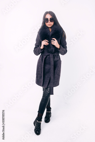 Lovely girl in a warm coat with a fur hood. Studio photography of winter clothing. Young adult girl in an elegant coat on a white background. Promotional womens coat. Coat with eco fur.