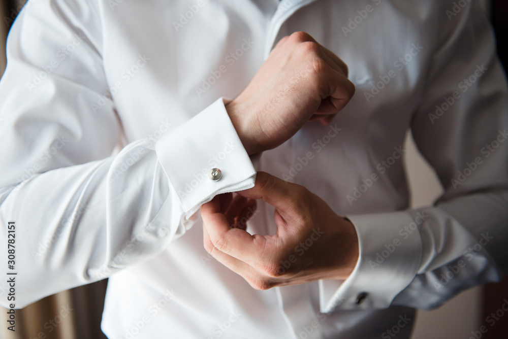 The groom fastens cufflinks on the cuffs of the white shirt. Close up The groom fastens cufflinks on the cuffs of the white shirt. Close up