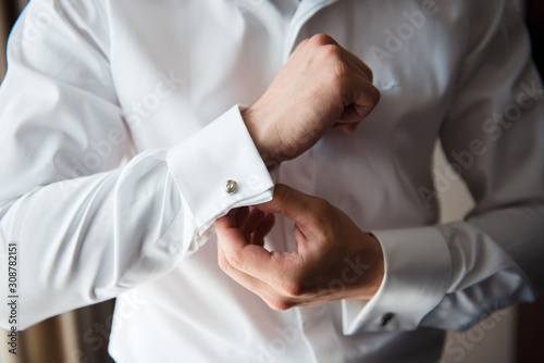 The groom fastens cufflinks on the cuffs of the white shirt. Close up