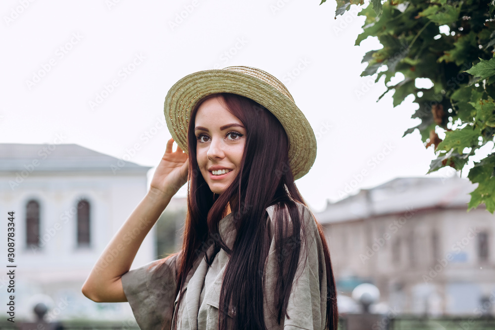 Cute brunette girl in a straw hat outdoors. close-up portrait of a young woman . Smiling girl walks around the city in the summer. Active spirit in the park.