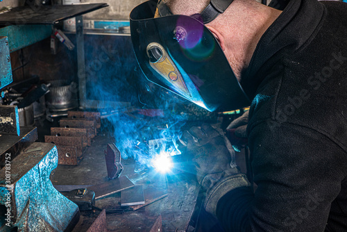 Worker in welding mask at factory. Welding process. Electric welding. Bright blue.