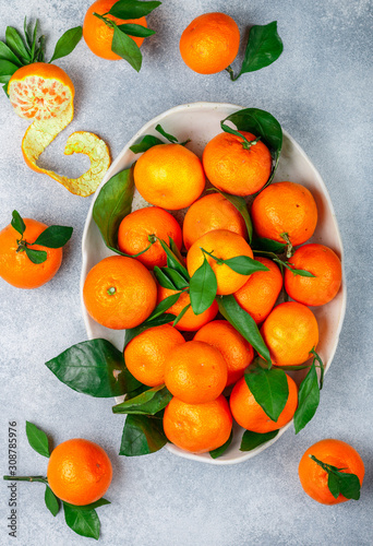 Fresh citrus mandarin oranges fruit (tangerines, clementines,) with leaves in a light dish on a gray stone or concrete background. Selective focus, top view and copy space © la_vanda