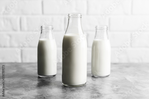 Three glass reusable bottles of milk in the kitchen with marble countertops and a white brick wall.