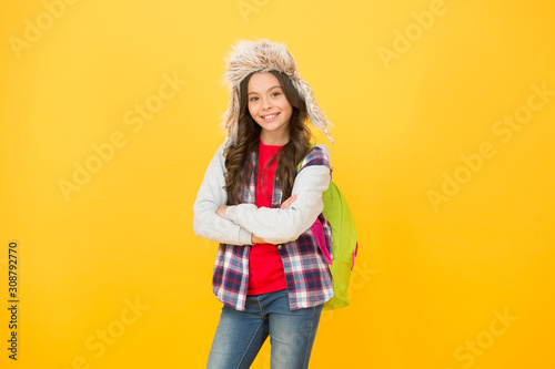 winter events at school. small girl wear earflap hat. winter school time and holidays. back to school. schoolgirl backpack yellow background. no classes this week. cheerful child pupil