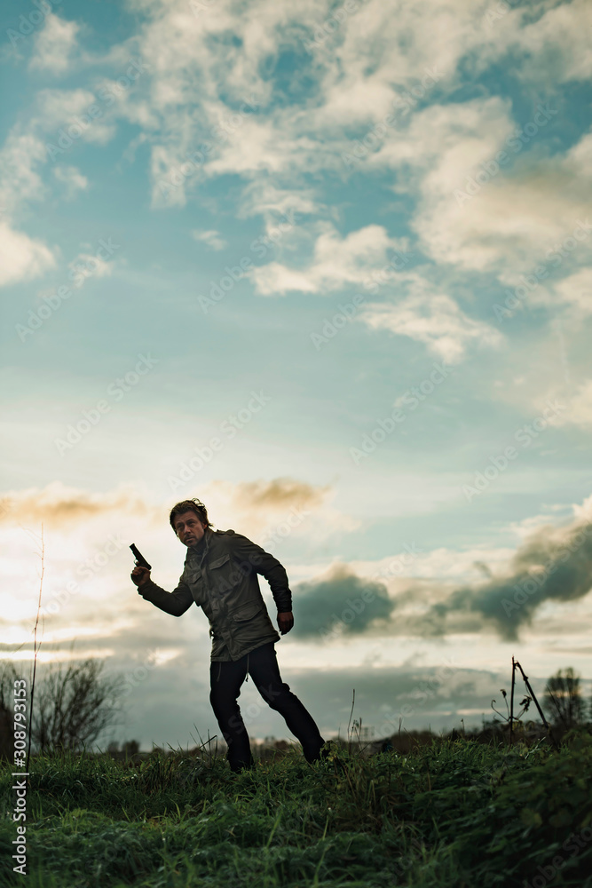 Man with pistol in countryside at sunset. Man with pistol in countryside at sunset.