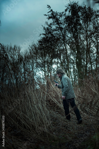 Man with pistol between reed on cloudy day. © ysbrandcosijn