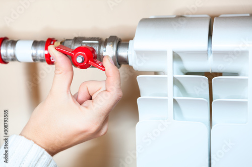 Female hands adjusting the red valve of central heating radiator