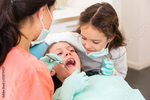 Cheerful female dentist with two little girls, playing assistant and patient
