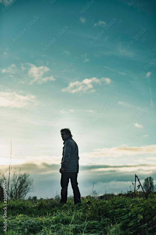 Mysterious man in rural landscape with cloudy sky at sunset.