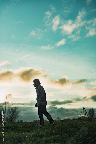 Mysterious man in rural landscape with cloudy sky at sunset.