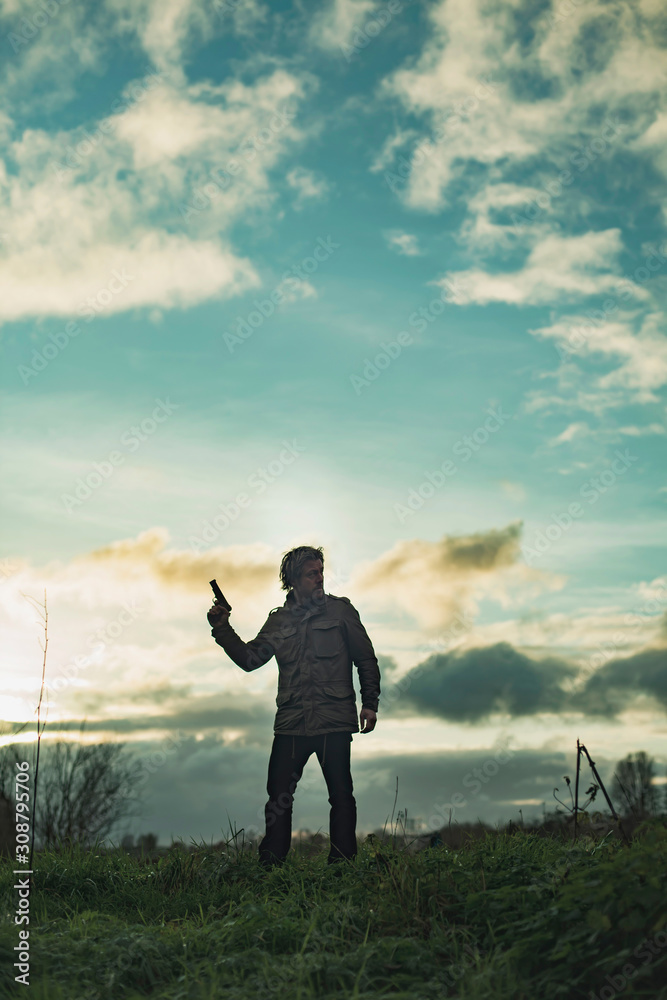 Man with handgun in countryside at sunset. Man with handgun in countryside at sunset.